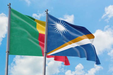 Marshall Islands and Benin flags waving in the wind against white cloudy blue sky together. Diplomacy concept, international relations.
