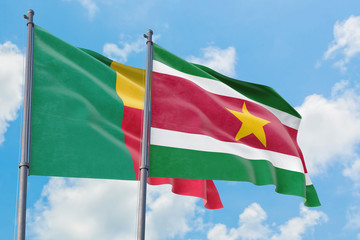 Suriname and Benin flags waving in the wind against white cloudy blue sky together. Diplomacy concept, international relations.