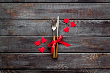 Valentines' Day dating in restaurant concept. Fork and knife decorated with hearts on wooden background top-down copy space