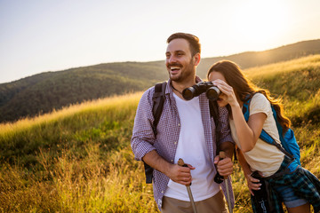 Happy couple is hiking in mountain. They are watching nature with binoculars.