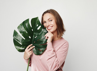 Beautiful young woman holding a leaf of a large tropical flower and smiling