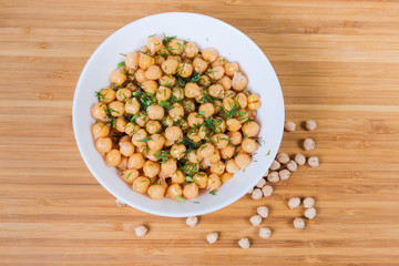 Boiled chickpeas in bowl on wooden surface with uncooked chickpeas