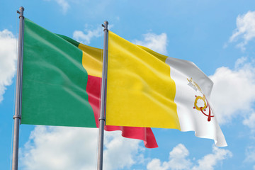 Vatican City and Benin flags waving in the wind against white cloudy blue sky together. Diplomacy concept, international relations.