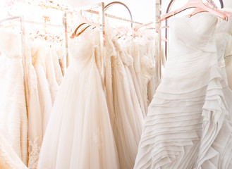 Beautiful, white bridal dress texture on background. Wedding dresses hanging on a hanger interior of bridal salon. Design, fashion modern luxury in detail. Soft  focus with warm light.