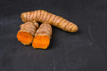 A halved and a whole fresh turmeric root on a black slate plate background.