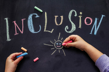 Word Inclusion on black school blackboard written with chalk. Children hands, education concept