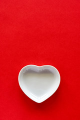 Valentine background. White porcelain heart on red background to be used as a template for valentine's day or wedding. Vertical image with copy space.