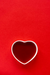 Valentine background. White porcelain heart filled with red liquid on a red background to be used as a template for valentine's day or wedding. Vertical image with copy space.