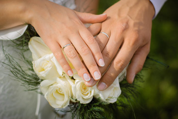 Obraz na płótnie Canvas Hands of the bride and groom with wedding rings on a wedding bouquet of white roses