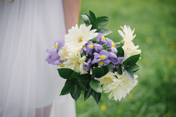 Beautiful wedding bouquet of milk gerberas and lilac irises in the bride's hand