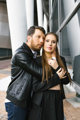 Stylish couple in love in business clothes near the glass wall of an office building, the guy hugs the girl's