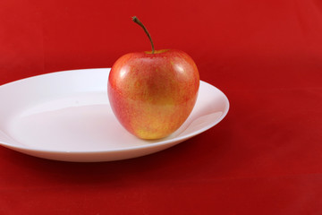 Red apple on a white plate on a red background.