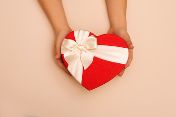 Children's hands hold gift box in the form of heart on beige background. A concept by the Mother's Day.  Father's day. Birthday.