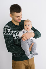 A young father holds his five-month-old son in his arms against a light background and smiles