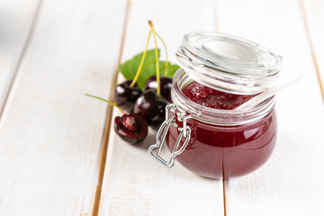 Cherry jam in glass jar, copy space, white wood background