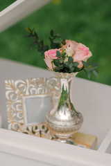 A small silver vase with pink rose flowers and green branches and a photo fram