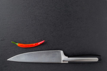 Sharp chef knife and fresh pod of red hot chili pepper on a black stone serving board. Mockup for menu design. Isolated on white. Copy space.