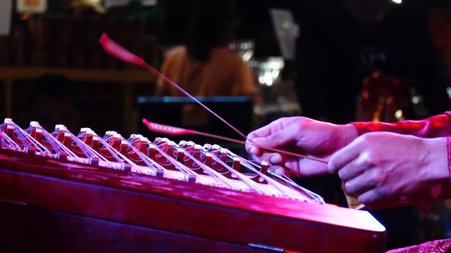 close up shot racks into focus on a man's hands playing a zither with sticks at a Chinese New Year performance.