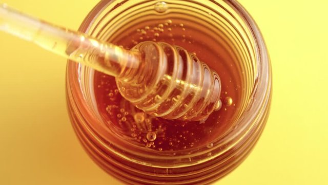 top view of honey pot full of honey and a transparent honey dipper spoon with honey pouring 