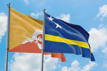 Curacao and Bhutan flags waving in the wind against white cloudy blue sky together. Diplomacy concept, international relations.
