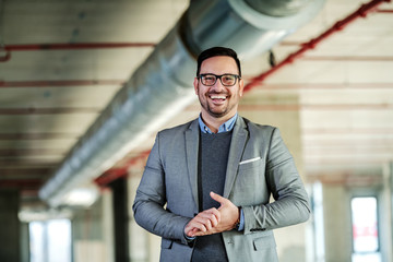 Obraz premium Smiling handsome caucasian businessman in suit is happy to present his own project while standing in building in construction process.