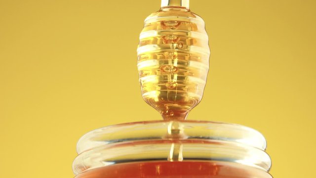 woman hand lifted up a honey pot tap with a honey dipper and a transparent honey pouring from spoon to jar