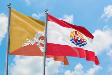 French Polynesia and Bhutan flags waving in the wind against white cloudy blue sky together. Diplomacy concept, international relations.