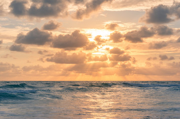 Sunrise seascape with colorful golden orange clouds and soft blue waves
