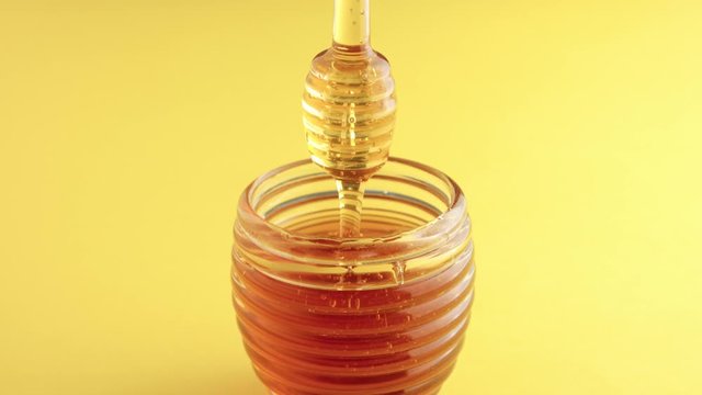 transparent honey jar in beehive shape and a honey dipper lifted up to see how honey pouring on jar