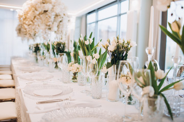 formal luxury elegant wedding decor restaurant tables served white tablecloth, plates, menus, glasses, tulips in vases, orchids, candles silver chairs, blue background