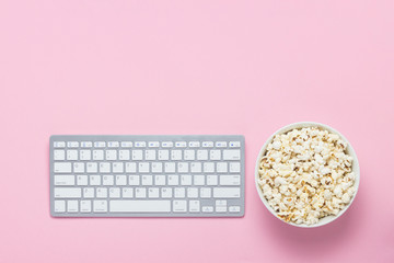 Keyboard and bowl of popcorn on a pink background. The concept of watching movies, TV shows and...