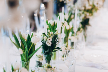 formal luxury elegant wedding decor restaurant tables served white tablecloth, plates, menus, glasses, tulips in vases, orchids, candles silver chairs, blue background