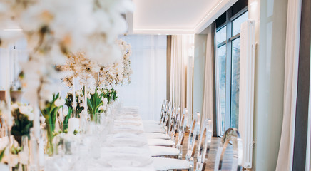 formal luxury elegant wedding decor restaurant tables served white tablecloth, plates, menus, glasses, tulips in vases, orchids, candles silver chairs, blue background