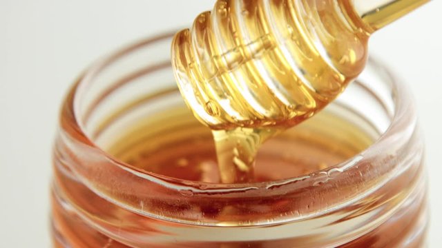 closeup of honey texture, transparent honey dipper lifted up from honey pot with pouring honey