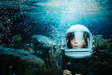 A small child dives underwater in a helmet and looks at a coral reef. Cartoon photo