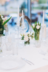formal luxury elegant wedding decor restaurant tables served white tablecloth, plates, menus, glasses, tulips in vases, orchids, candles silver chairs, blue background