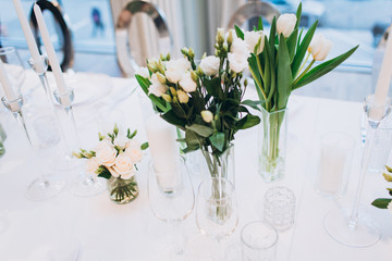 formal luxury elegant wedding decor restaurant tables served white tablecloth, plates, menus, glasses, tulips in vases, orchids, candles silver chairs, blue background