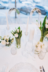 formal luxury elegant wedding decor restaurant tables served white tablecloth, plates, menus, glasses, tulips in vases, orchids, candles silver chairs, blue background