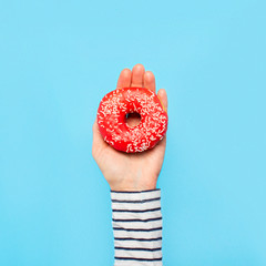 Female hand holds a donut on a blue background. Concept confectionery store, pastries, coffee shop....