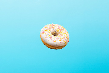 Flying in air donut with white icing on a blue background. Bakery, baking concept. Levitation