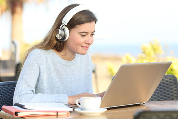 Student e-learning with headphones and laptop in a bar