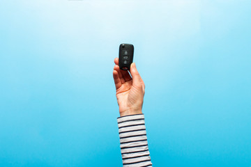 Female hand holds car keys on a blue background. Concept car, car rental, gift, driving lessons, driving license. Banner. Flat lay, top view