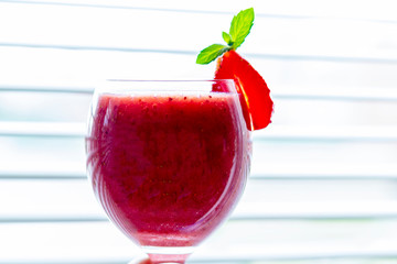 Fresh iced strawberry smoothie in wine glass decorated with slice of strawberry and mint against...