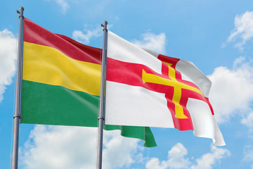 Guernsey and Bolivia flags waving in the wind against white cloudy blue sky together. Diplomacy concept, international relations.