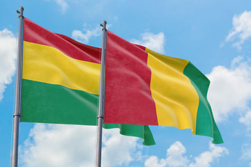Guinea and Bolivia flags waving in the wind against white cloudy blue sky together. Diplomacy concept, international relations.