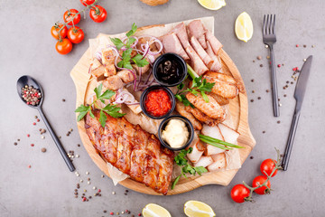 The meat plate is filled with cuts and steaks, supplemented with sauces, decorated with herbs, cherry tomatoes and lemons. The concept of meat or beer appetizer.