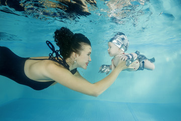 Mom with a little son smiling dives underwater in a swimming pool