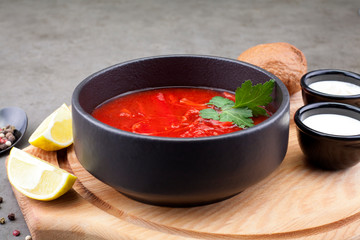 Tomato soup with vegetables, decorated with parsley, in a black plate, on a wooden Board, decorated with tomatoes and onions. Concept soups or healthy food.