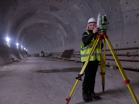 Pretty young mining surveyor woman works on the geodetic total station in the tunnell of metro under construction