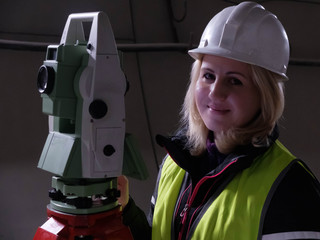 Portrait of pretty young mining surveyor woman in hardhat standing by geodetic total station in the...